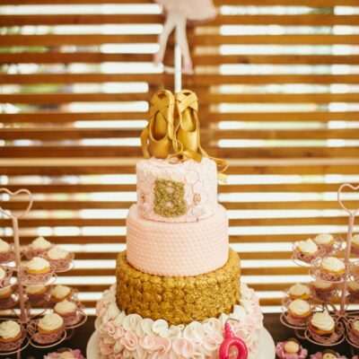 Delicious birthday cake decorated with edible pointe shoes placed on festive table against wooden wall