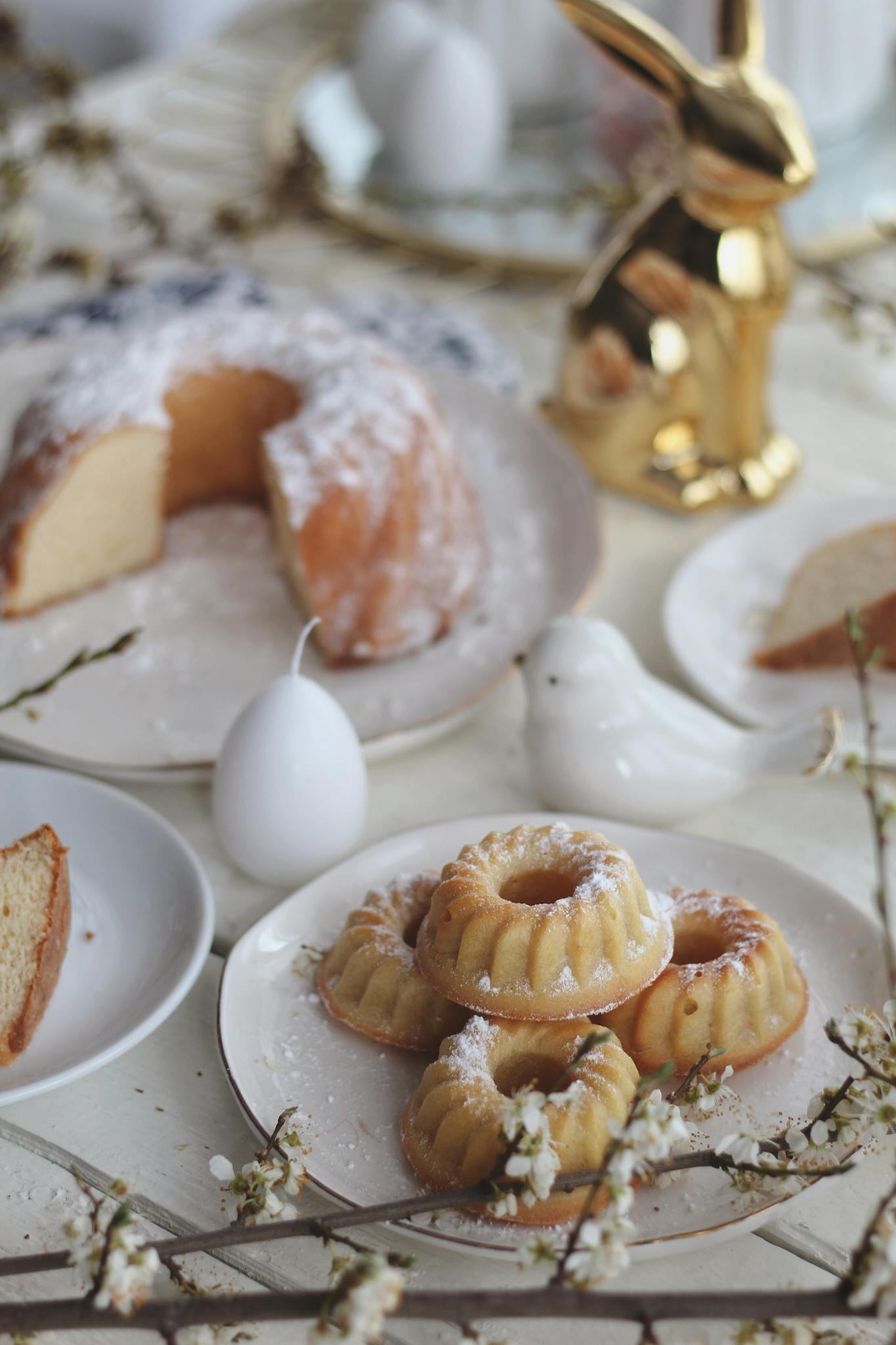 Plates with tasty fresh bundt cakes served on table with Easter egg and bunny in light room during holiday celebration