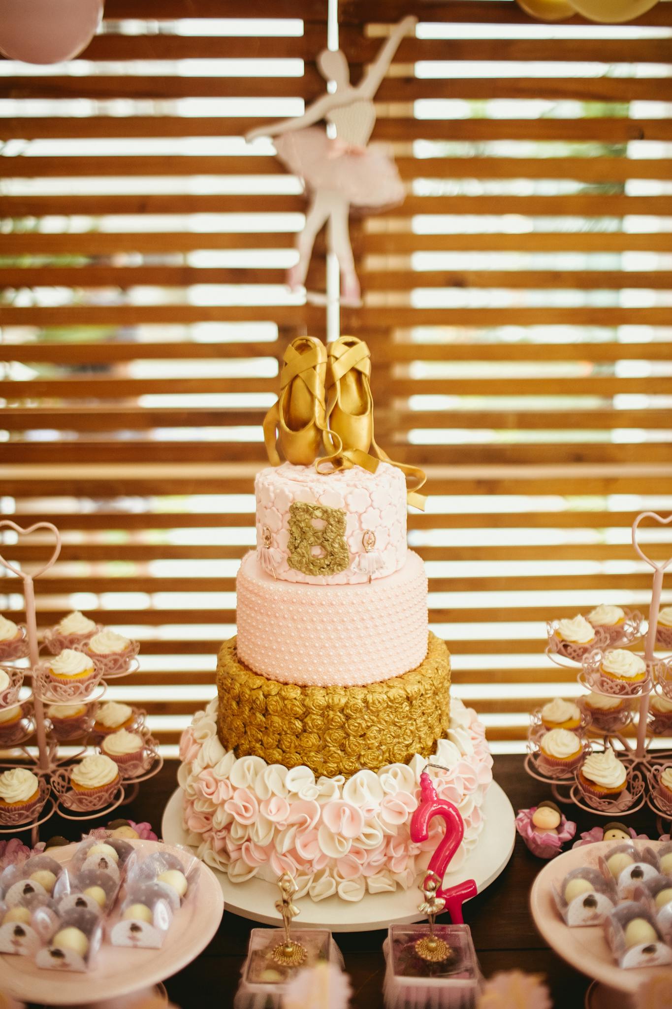 Delicious birthday cake decorated with edible pointe shoes placed on festive table against wooden wall